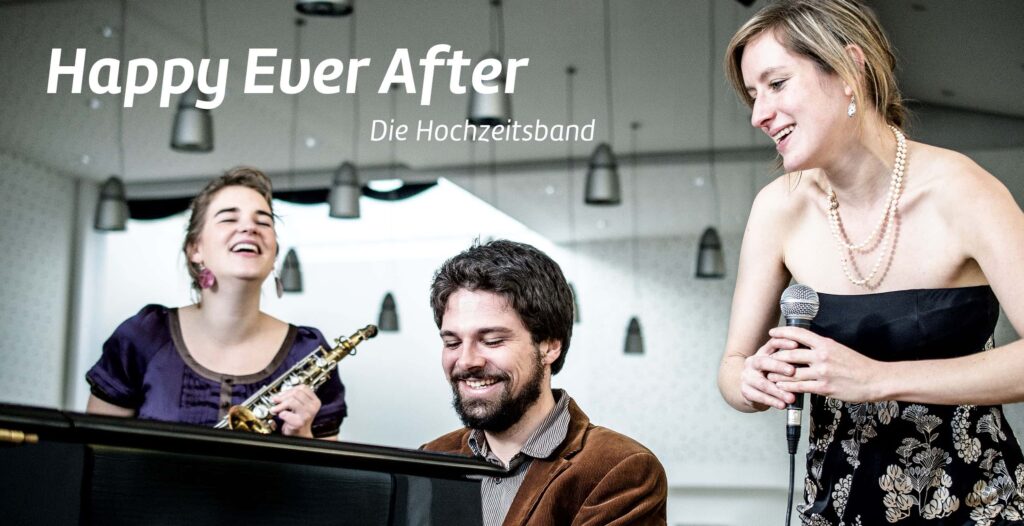 Drei Musiker spielen fröhlich in einer Halle; eine Frau singt in ein Mikrofon, ein Mann spielt Klavier, und eine andere Frau lächelt mit ihrer Klarinette. Der Text über dem Bild lautet "Happy Ever After - Die Hochzeitsband", präsentiert von Webdesign Aachen.
