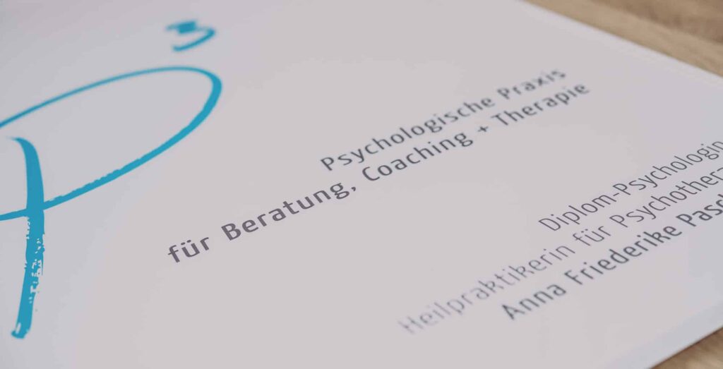 Nahaufnahme eines Dokuments mit deutschem Text über psychologische Praxis, Beratung, Coaching und Therapie, mit dem Namen "Anna Friederike Passlack" auf weißem Hintergrund mit einem blauen Grafikelement. Stichworte sind Webdesign Aachen.