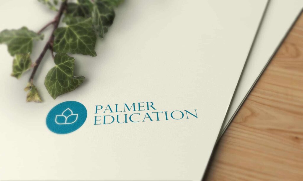 Ein Blatt Papier mit dem blauen Logo und dem Schriftzug "Palmer Education" liegt auf einer hölzernen Fläche, teilweise verdeckt von einer grünen Efeupflanze - eine inspirierende Szene für jeden Webdesigner Aachen.
