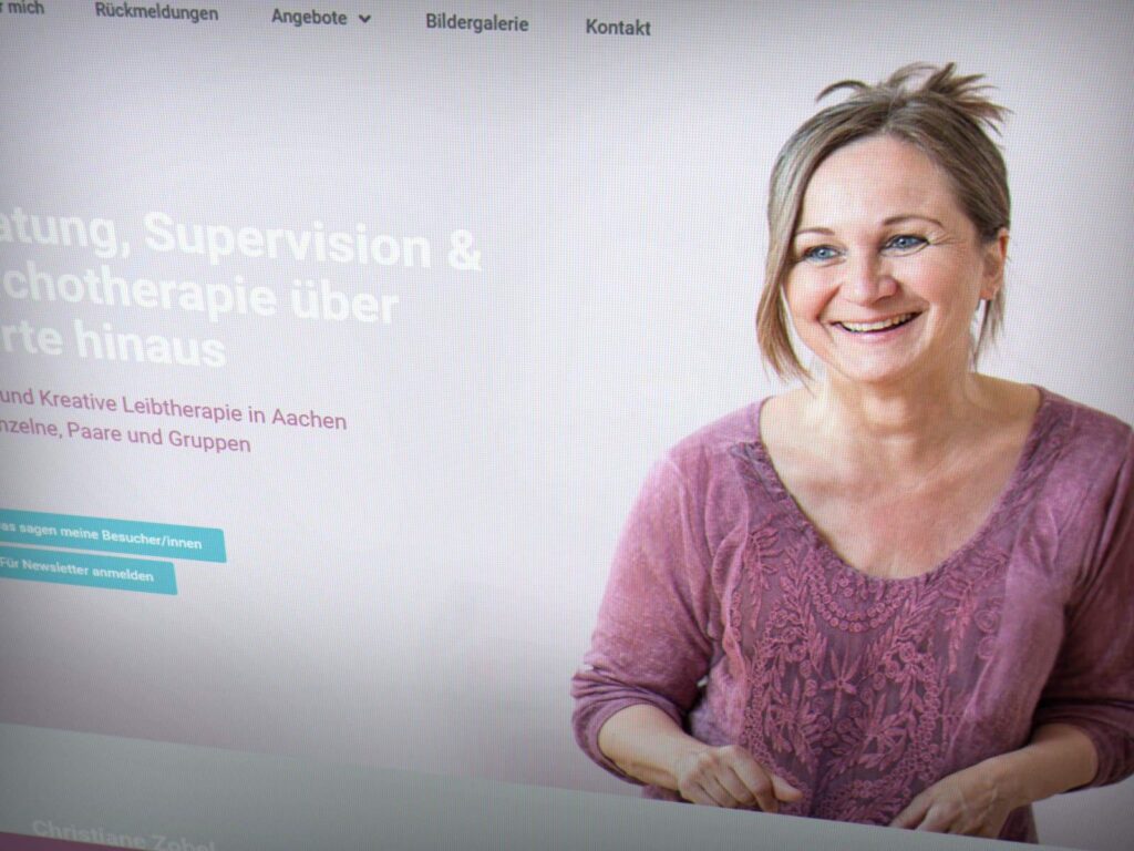 Eine lächelnde Frau mit hellbraunem, zurückgebundenem Haar und lila Bluse ist auf einer Website für Beratungsdienste zu sehen. Auf der Website, die von einem Aachener Webdesigner erstellt wurde, befinden sich das Menü und eine Schaltfläche zur Anmeldung auf der linken Seite.