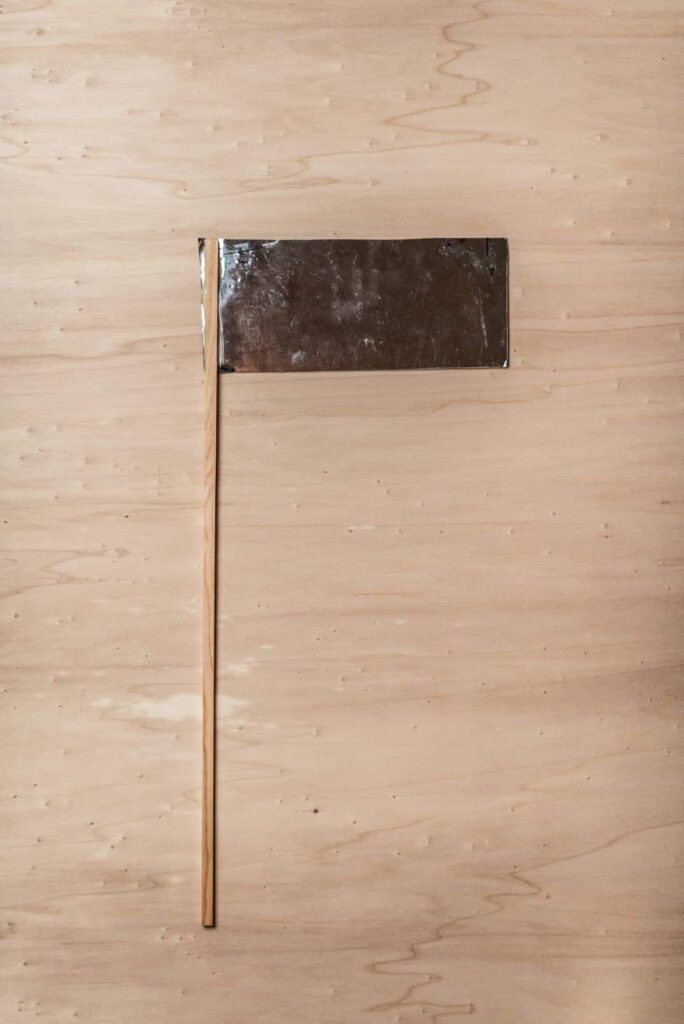 Ein rechteckiges Metallschild mit einem Holzstabgriff steht senkrecht auf einer hellen Holzfläche und erinnert an ein leeres Protestplakat - die perfekte Inspiration für jedes Webdesign Aachen-Projekt.