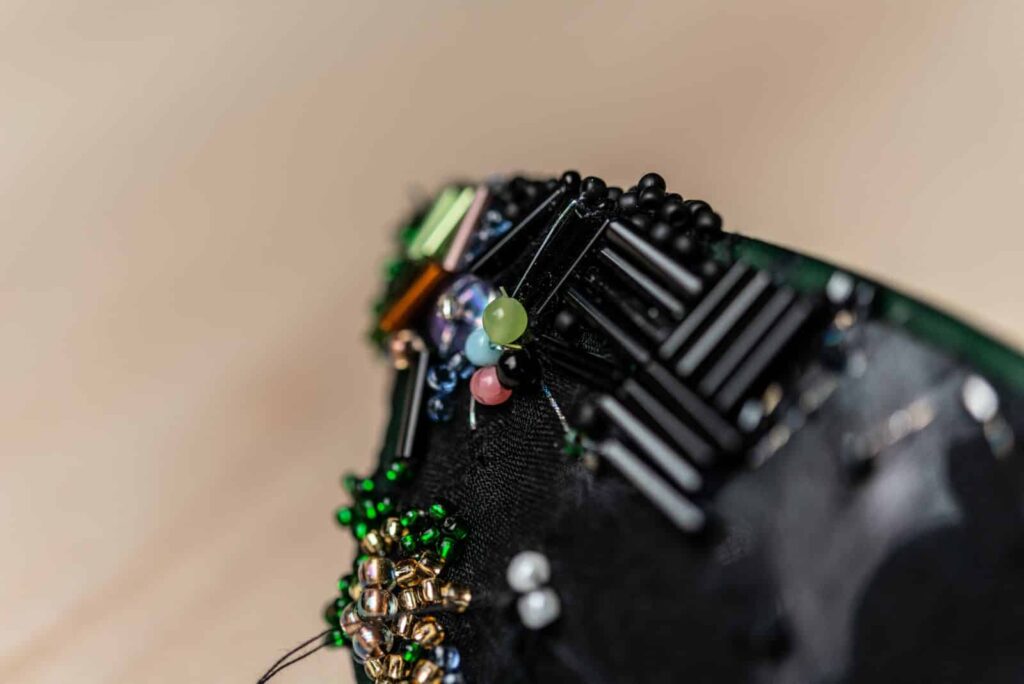 Nahaufnahme eines schwarzen Stoffes, der mit grünen, rosafarbenen, goldenen und schwarzen Perlen in einem strukturierten Muster verziert ist - eine Reminiszenz an die detaillierte Handwerkskunst, die von den Profis des Webdesigners Aachen geschätzt wird.