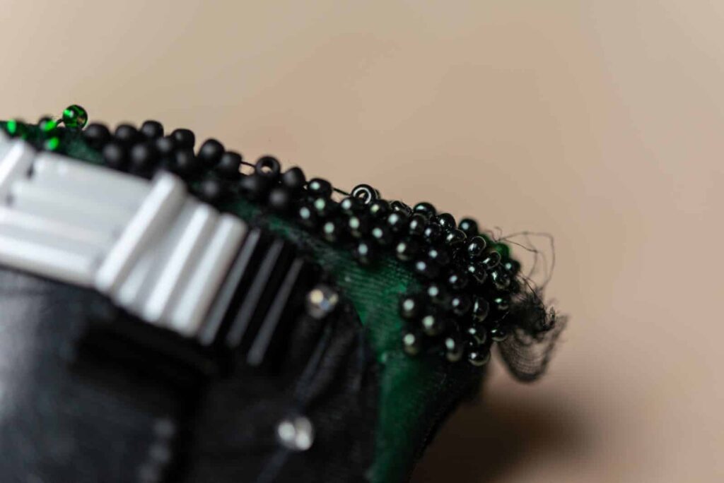 Nahaufnahme eines dekorativen Objekts mit kleinen schwarzen und grünen Perlen, die auf dunkelgrünem Stoff befestigt sind, zusammen mit silbernen und schwarzen rechteckigen Elementen - eine kreative Note, die an herausragende Projekte von Webdesign Aachen erinnert.