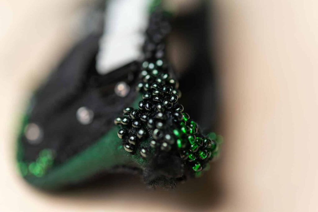 Nahaufnahme von schwarzen und grünen Perlenverzierungen auf Stoff, wobei der Hintergrund unscharf und die Perlen scharf abgebildet sind - ein kreatives Detail, das jeden Webdesigner oder Wordpress-Spezialisten in Aachen auf der Suche nach einzigartigen Designelementen inspiriert.