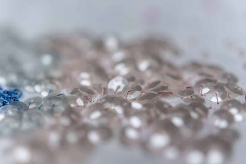 Eine verschwommene Nahaufnahme von kleinen, durchsichtigen Perlen, die auf einer Oberfläche verstreut sind, mit Andeutungen von Blau und Weiß - die perfekte abstrakte Inspiration für jedes Webdesign Aachen oder Wordpress Aachen Projekt.