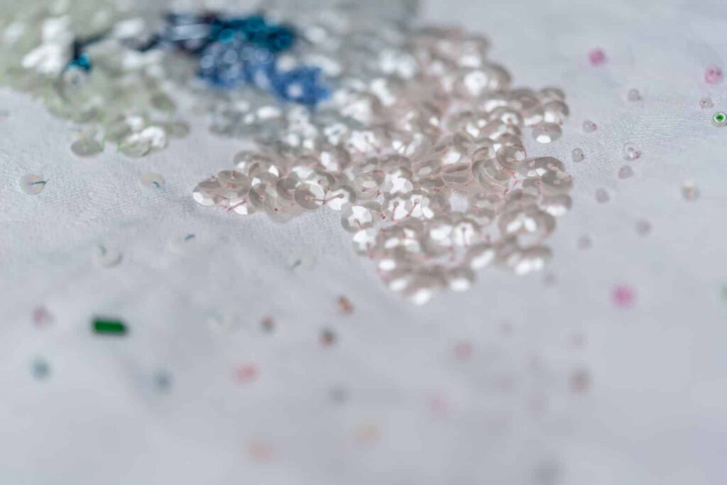 Nahaufnahme von glänzenden, schillernden Pailletten und Perlen, die auf einer weißen Stoffoberfläche verstreut sind, mit einigen Bereichen im Weichzeichner - die perfekte Inspiration für Webdesign Aachen oder jedes kreative Wordpress Aachen-Projekt.