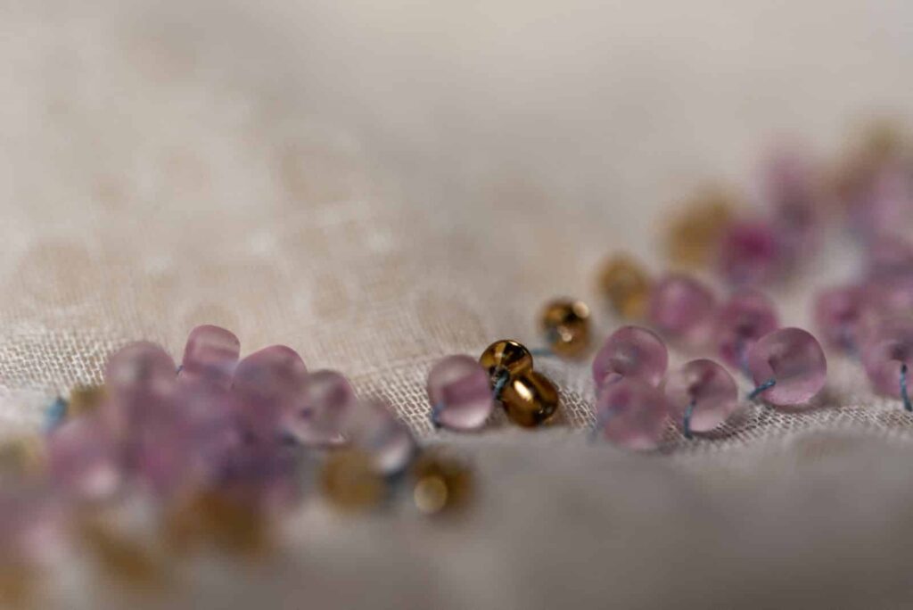 Nahaufnahme von kleinen, runden, durchscheinenden lila Perlen und glänzenden goldenen Perlen, die auf einer leichten, strukturierten Stoffoberfläche verstreut sind. Perfekt für ein Webdesign Aachen Projekt. Der sanft verschwommene Hintergrund lenkt den Fokus auf die lebendigen Perlen im Vordergrund.