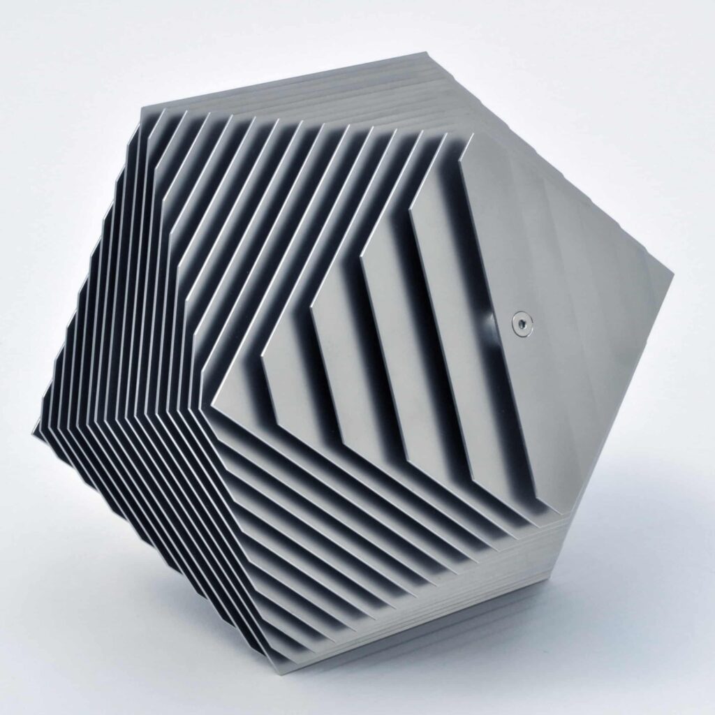 Eine geometrische Skulptur mit einer metallischen, sechseckigen Form mit gleichmäßig verteilten, parallelen Lamellen erzeugt einen geschichteten, dreidimensionalen Effekt - ein inspirierendes Stück für jeden Webdesign Aachen- oder kreativen Wordpress Aachen-Arbeitsbereich.
