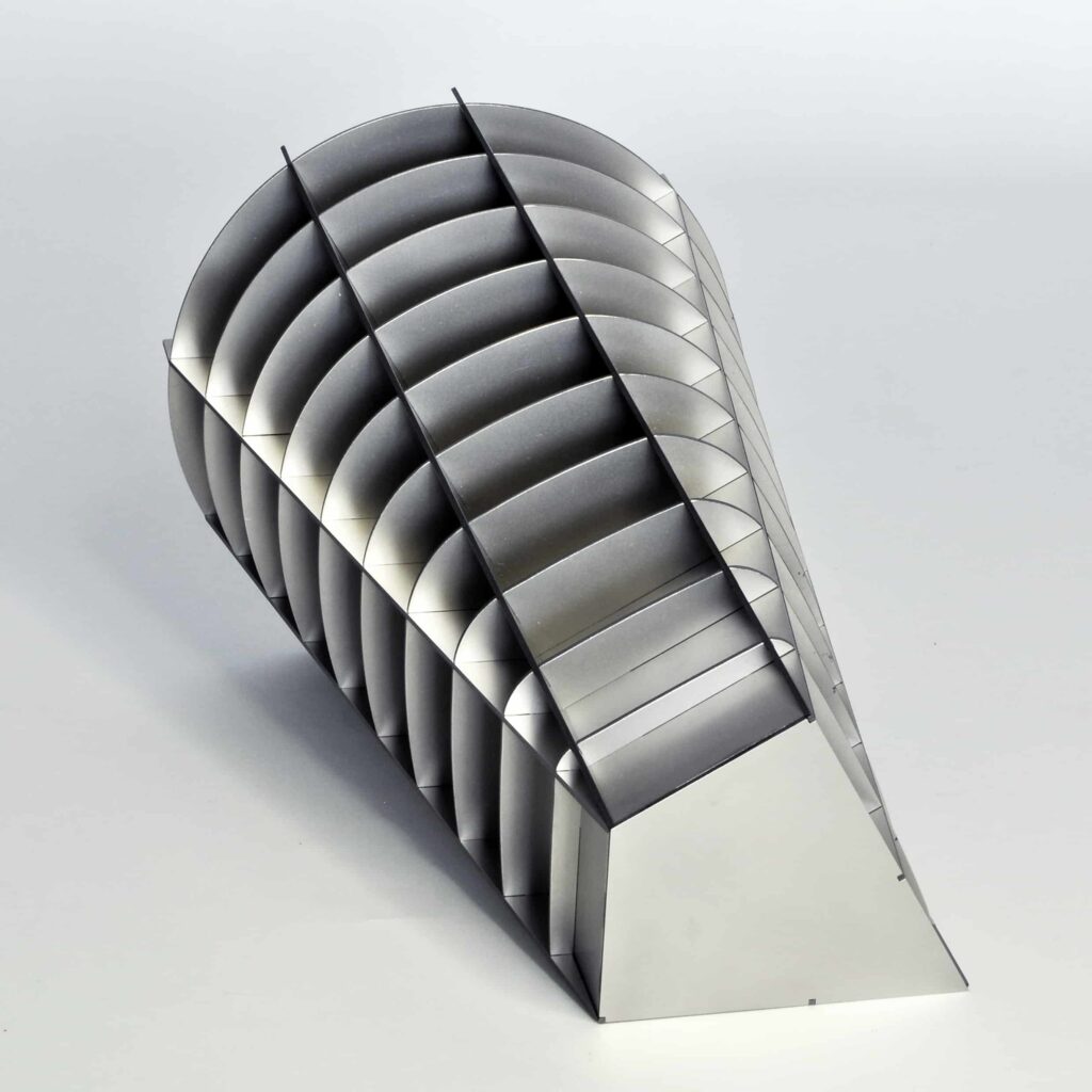 Eine geometrische Metallskulptur mit gebogenen, gerippten Segmenten, die eine kegelförmige Form bilden, die an einem Ende breiter ist und am anderen Ende spitz zuläuft, dargestellt auf einem schlichten weißen Hintergrund - die perfekte Inspiration für moderne Webdesign Aachen Projekte.