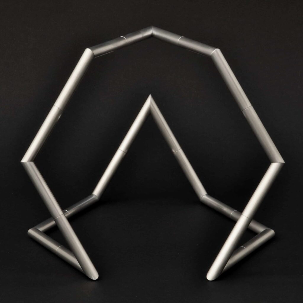Eine geometrische Skulptur aus silbernen Metallrohren, die in kantigen, miteinander verbundenen Formen angeordnet sind und einen abstrakten, hausähnlichen Umriss auf schwarzem Hintergrund bilden - die perfekte Inspiration für modernes Webdesign Aachen.
