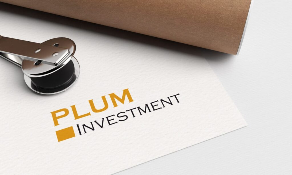 Ein Papier, das mit dem Logo "PLUM INVESTMENT" in gelber und schwarzer Schrift gestempelt ist, zusammen mit einem Metallstempelwerkzeug und einem braunen gerollten Dokument - die perfekte Inspiration für jedes Webdesign Aachen oder kreative Wordpress Aachen Projekt.