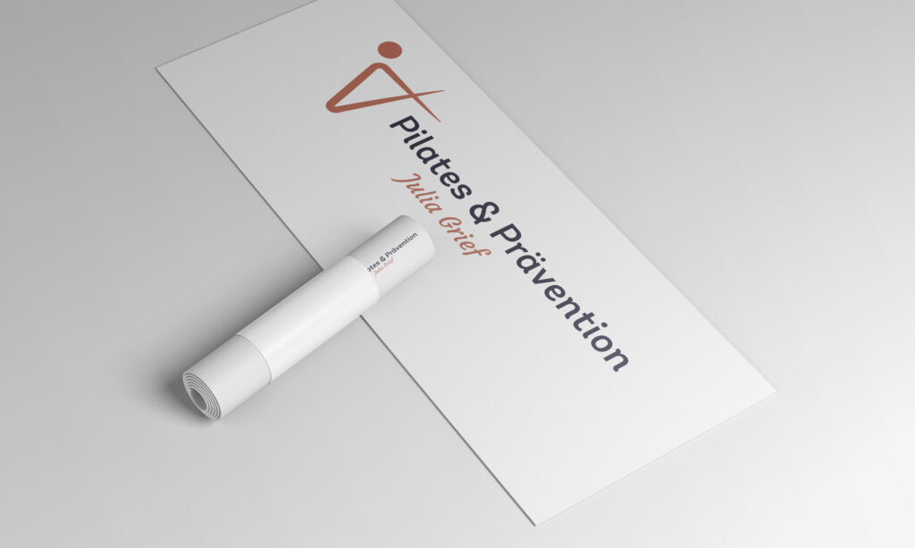 Eine weiße Yogamatte mit dem Aufdruck „Pilates & Prävention Julia Grief“ und einem minimalistischen Logo in Form einer menschlichen Figur liegt teilweise ausgerollt auf einem hellen Untergrund.