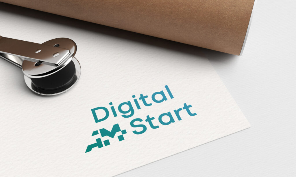 Ein Stück Papier mit dem türkisfarbenen und grünen "Digital Start"-Logo, das ein geometrisches Muster aufweist, wird neben einem Metallstempel und einem aufgerollten braunen Blatt gezeigt.