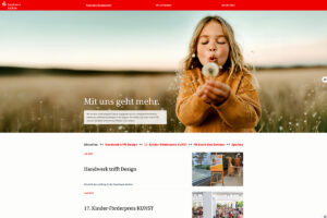 Ein junges Mädchen pustet auf einer sonnigen Wiese auf einen Löwenzahn. Die Website der Sparkasse Aachen, einem Finanzinstitut, enthält ein Navigationsmenü und aktuelle Nachrichten auf Deutsch.